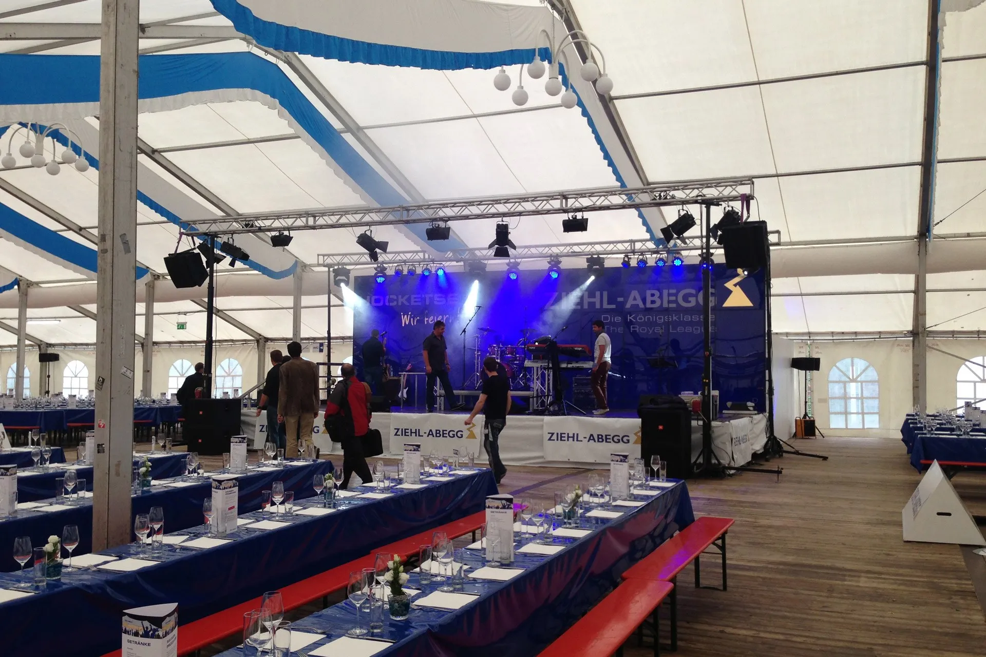 Festzelt mit Bühne, Traversen, Bühnenlicht und langen gedeckten Tischreihen