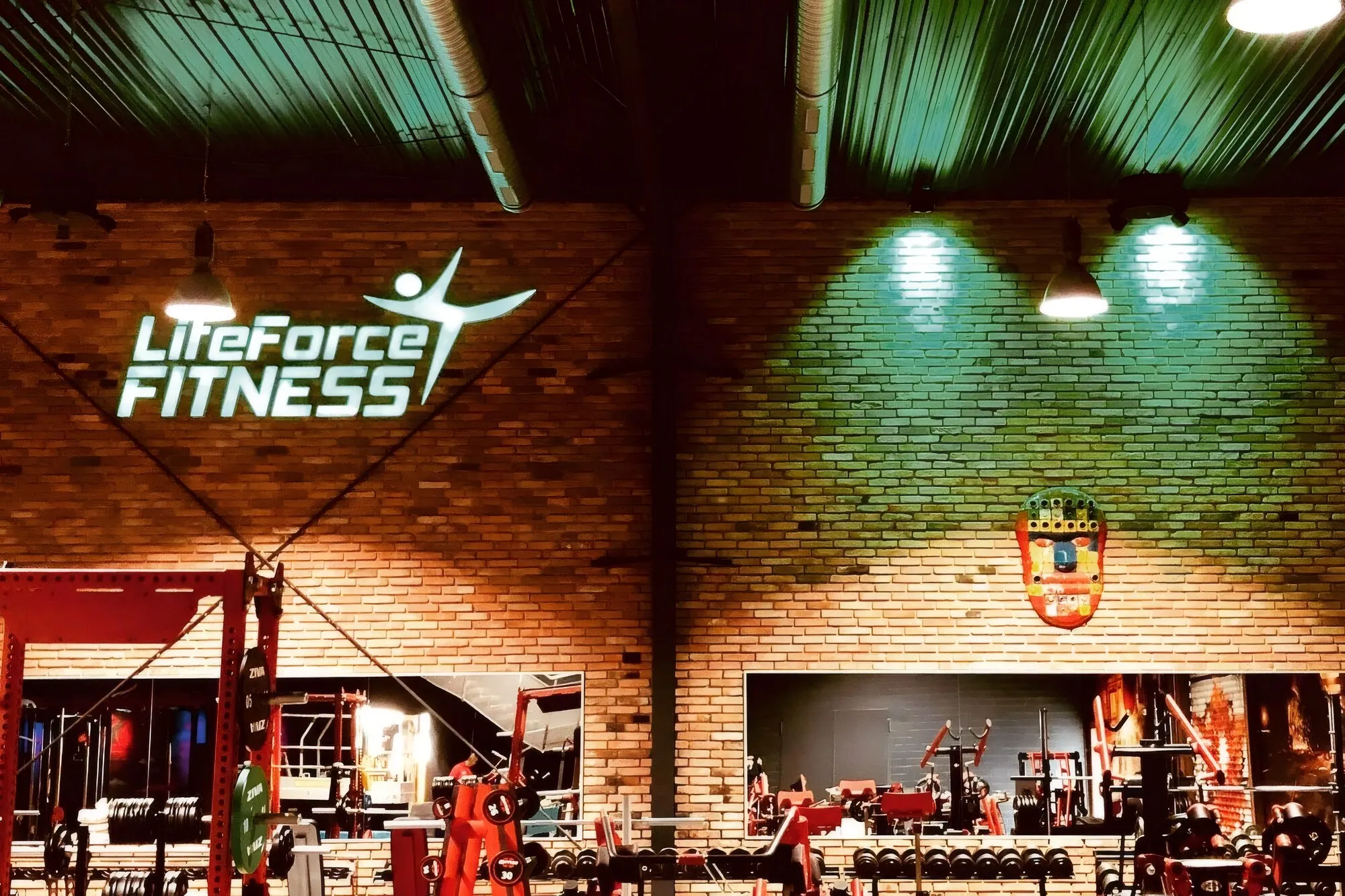 Fitnessstudio in einer Industriehalle mit Ziegelwänden, farbiger Beleuchtung und Trainingsgeräten